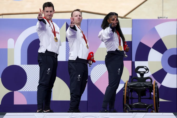 Three GB cyclists on the podium pointing at the camera making gun fingers