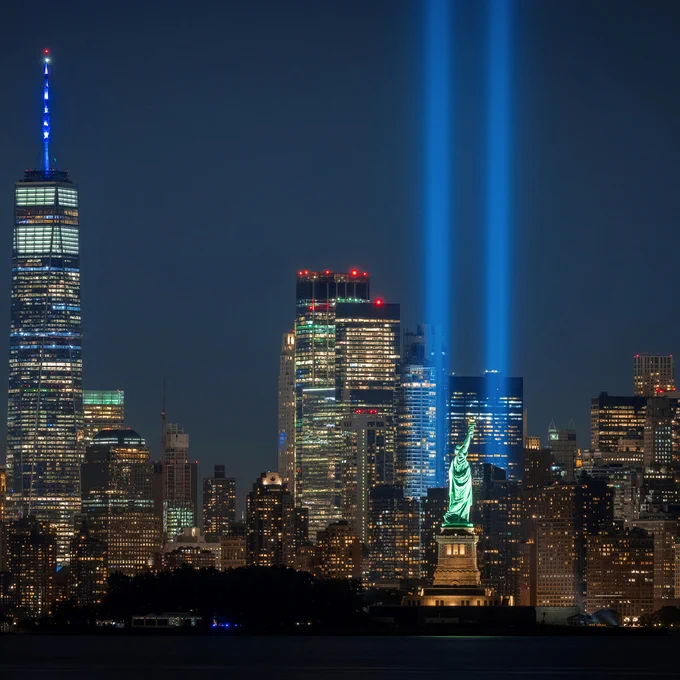 New York City at night showcasing lights from the 9/11 memorial in remembrance of the twin towers with the statue of liberty in frame.