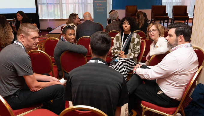 A group of individuals engaged in a discussion while seated in a circle at a conference.