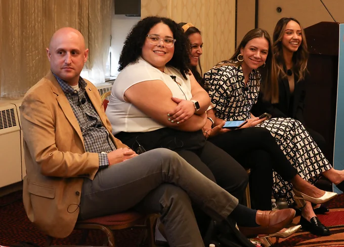 Five individuals sitting side by side, smiling at a conference.