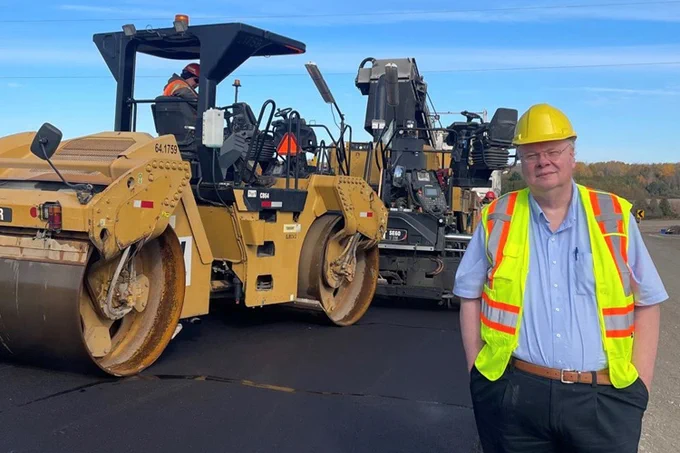 Dr. Simon Hesp standing in front of heavy road construction machinery.