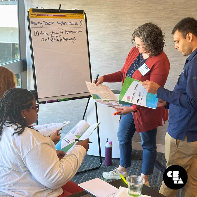 Four standards writers refer to the Reimagining CS Pathways report as they write ideas down on a post-it board.