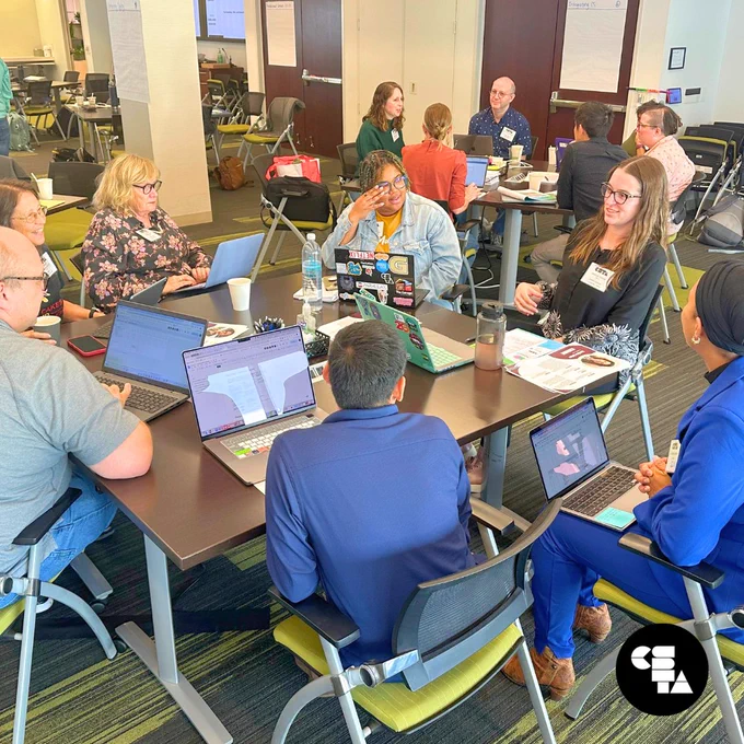 Standards writers are separated into two groups. Each group sits around a table facing their group mates with laptops out, participating in discussion. 