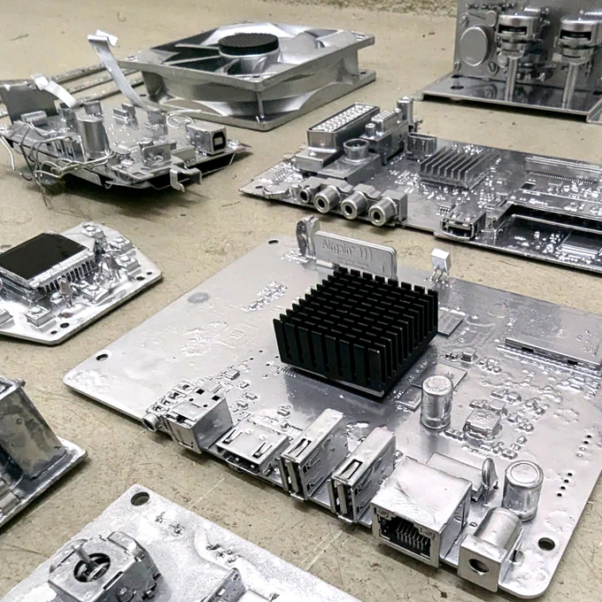 Intricate electronic circuit boards that have been coated in a reflective metallic finish; a variety of components, including capacitors, resistors, wires, and heat sinks, arranged on the boards; some boards stand vertically, while others lie flat on the floor; a noticeable detail is the silver wiring and gear mechanisms connecting some of the parts; the boards appear to be custom-built, likely crafted with attention to detail and technical precision, as they resemble modern electronics but with a polished, industrial aesthetic.