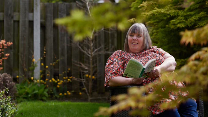 Woman sitting in a garden holding a book.