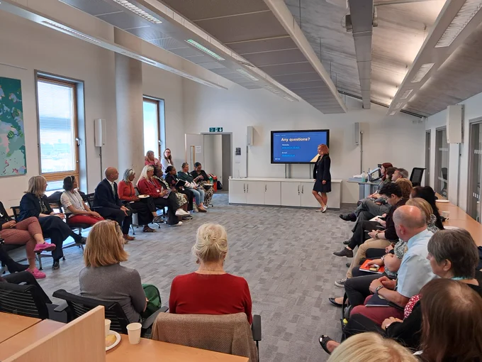 Prof Miranda Horvath standing at the front of a room and presenting to a room of seated delegates