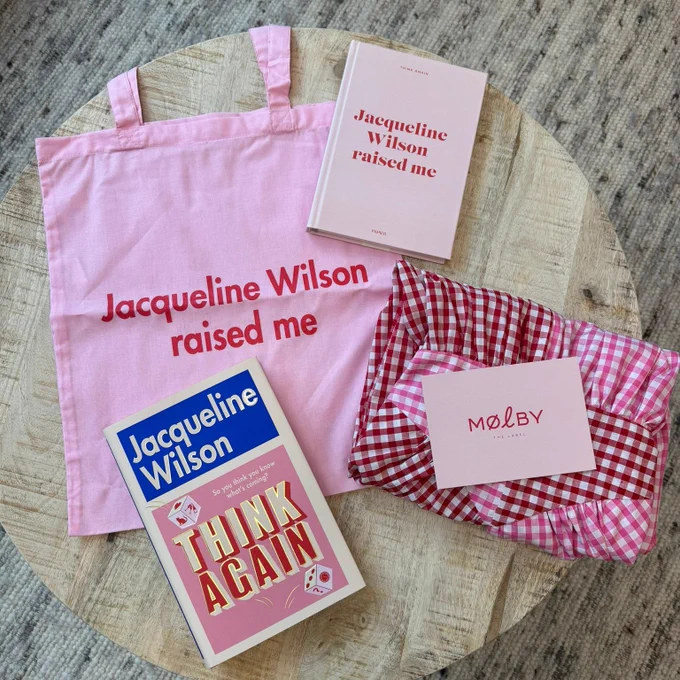 A photo of a pink tote bag and notebook with 'Jacqueline Wilson raised me' in red, a copy of Think Again, and a folded pink, red and white Molby the Label dress. 