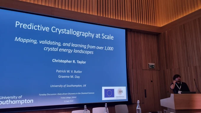Chris Taylor presenting at front of lecture theatre, with slide entitled Predictive Crystallography at Scale