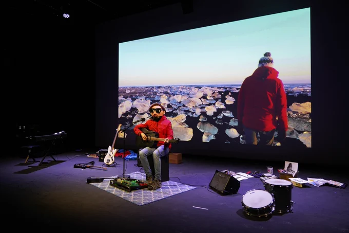 Promotional photo for A Version of Life - Man in mask playing guitar surrounded by musical equipment in front of a projected screen