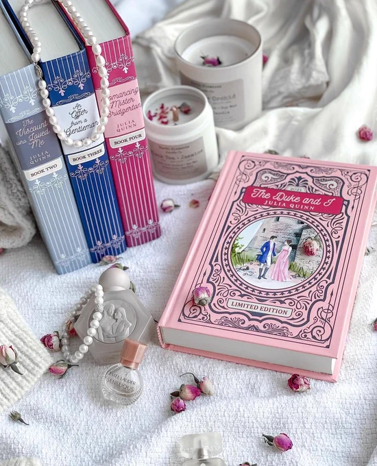 bridgerton books 1-4 on a white blanket with candles, pink flowers, perfume bottle