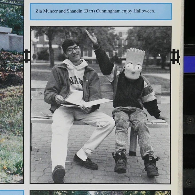 A yearbook page showing two students sitting on a bench together in the Fall on campus. The student on the right wears a Bart Simpson mask.
