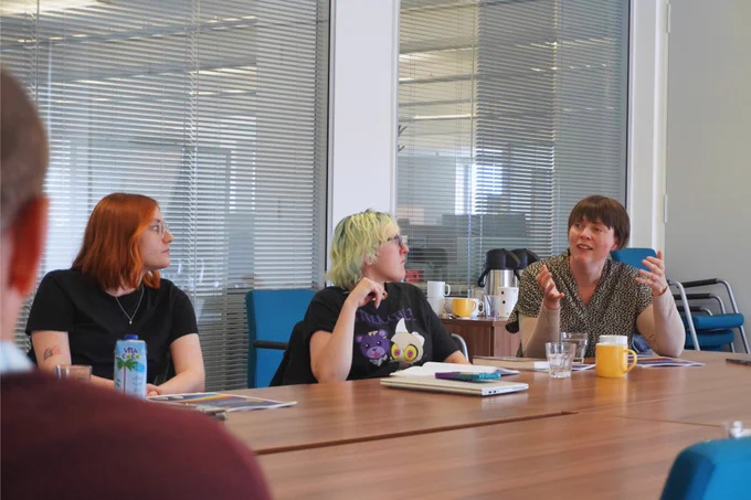Photo of Reb and two others in discussion. They are sitting around a table.