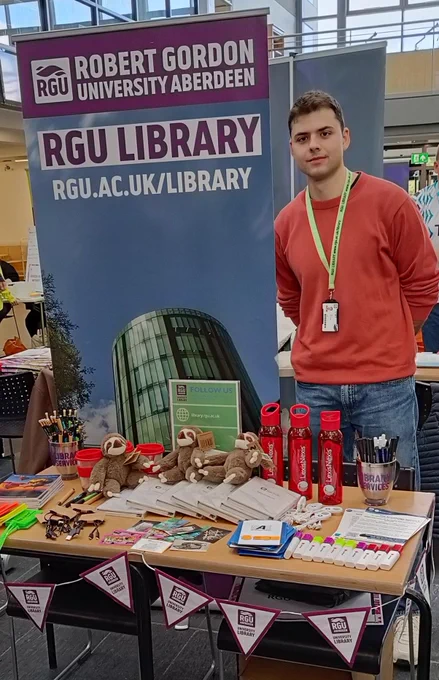 A library assistant waiting to give away lots of freebies from electronic resource providers at Freshers Fair stall