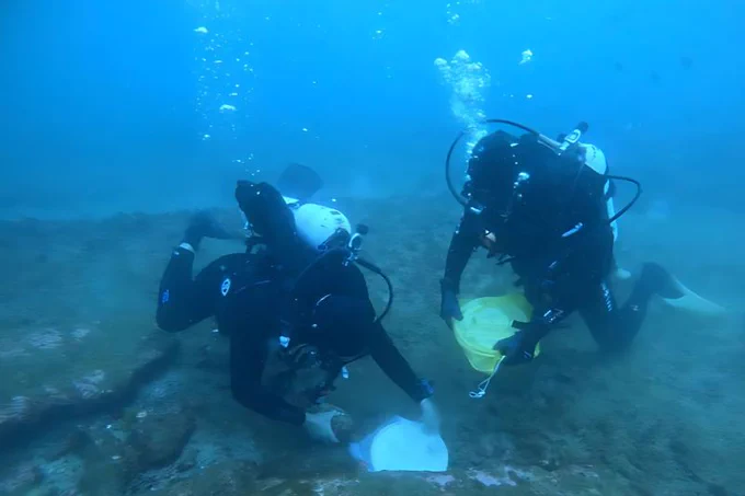 Two scuba divers are examining a submerged object on the ocean floor, surrounded by bubbles and blue water.

Researchers use a new technique called SMIRC to collect microbial natural products.