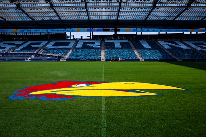View of an empty Children's Mercy Park stadium, featuring a large, colorful University of Kansas Jayhawks logo painted on the grass.