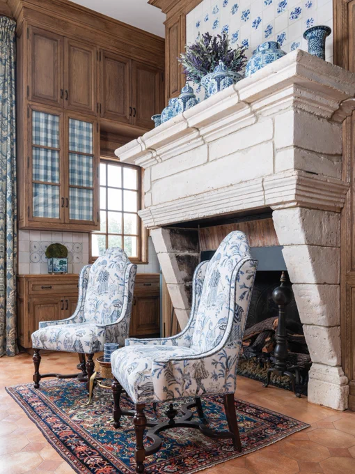 Second: The other side of the kitchen, with an oversize fireplace, delft tiles on the mantel, a Persian rug, and chairs upholstered in a medieval toile fabric.
