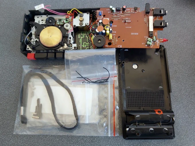 Photo of a disassembled micro cassette recorder. In the middle is a bag with fragments of a belt drive.