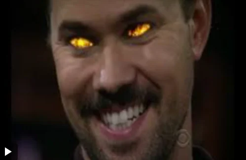 A close up of Andrew Rannells playing Darren in How I Met Your Mother. He has flames in his eyes and is grinning evilly.
