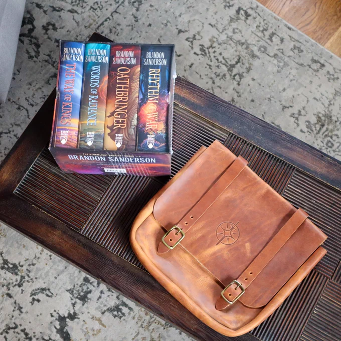 A photo of the Stormlight Archives by Brandon Sanderson Hardcover Box Set and one handmade Stormlight Archive themed tote bag are on a wooden table  