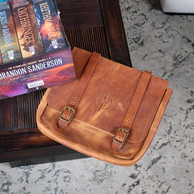 A photo of the Stormlight Archives by Brandon Sanderson Hardcover Box Set and one handmade Stormlight Archive themed tote bag are on a wooden table  