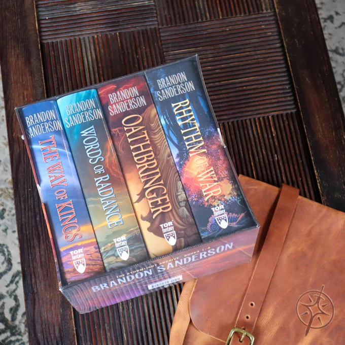 A photo of the Stormlight Archives by Brandon Sanderson Hardcover Box Set and one handmade Stormlight Archive themed tote bag are on a wooden table  