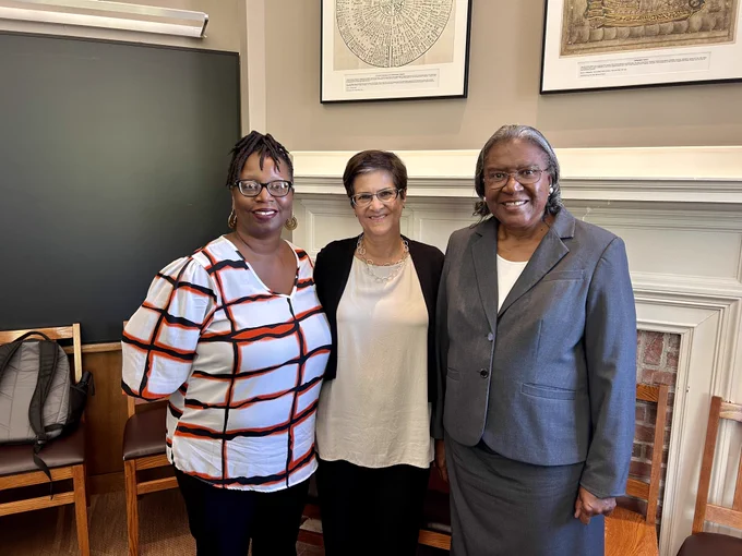 Three women stand together side by side smiling at the camera