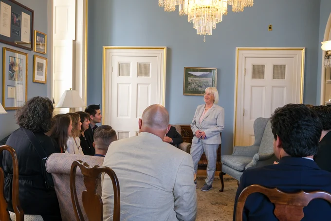 Senator Murray is standing and smiling to the left of the frame. Ten people are sitting around her in couches and chairs. They are sitting in a blue office with gold accents on the doorways.
