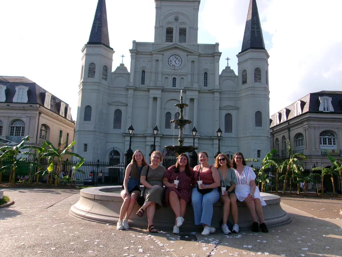 6 women sit on a fountain outside the church in Jackson Square.