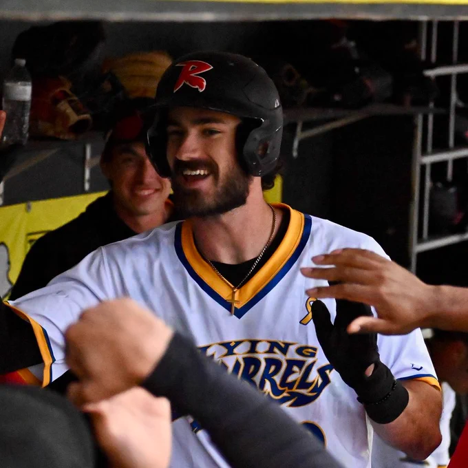 Bryce Eldridge smiles in the dugout while wearing a white uniform top with yellow trim.