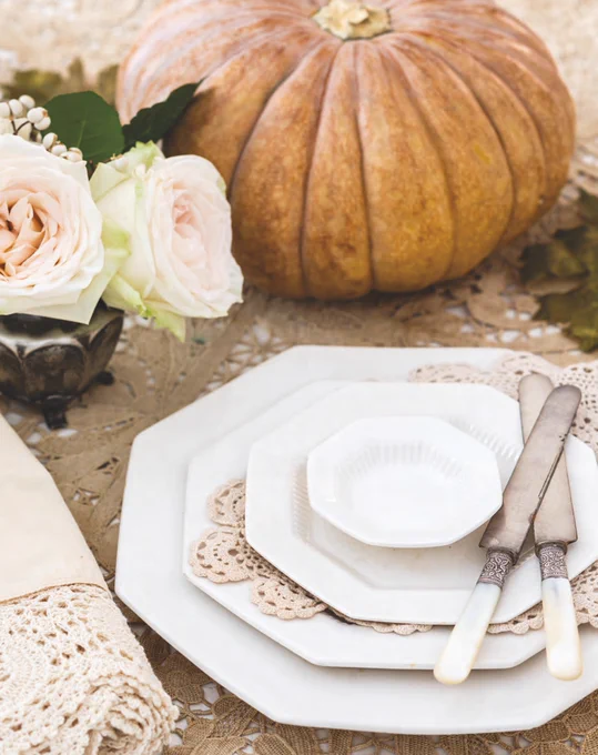 A place setting with octagonal ironstone plates, roses, and a pumpkin.