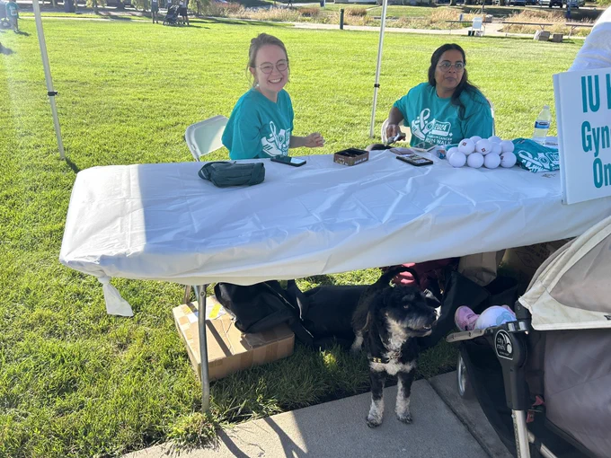 Two women sit at a table while a dog beneath it.