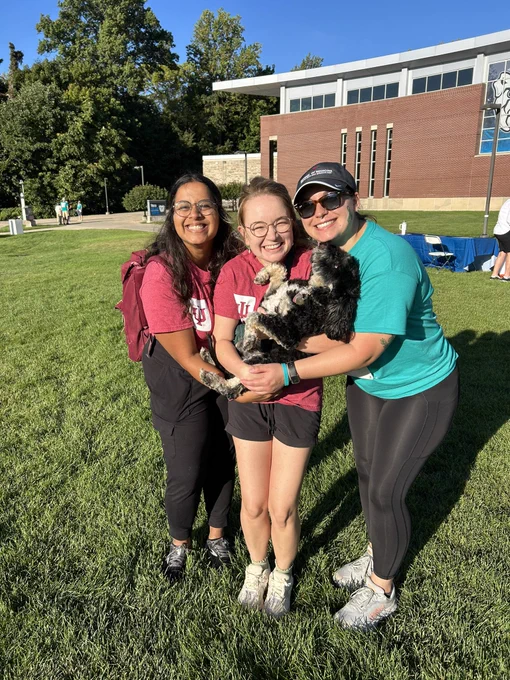 Three women smile while holding a dog