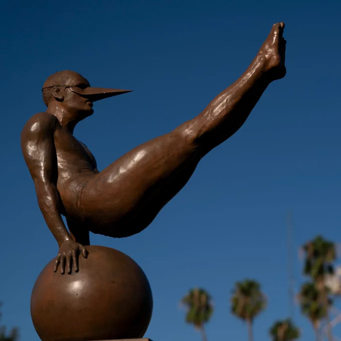 Sculture of masked human-like creature balancing on his hands on a ball.