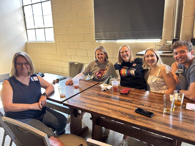 A group of people smile for a photo while sitting around a large wood table