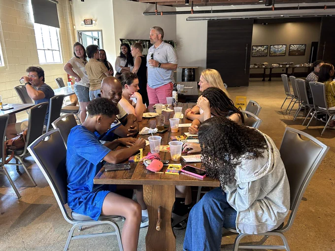 A group of people sit at a table smiling and talking while children at the table color