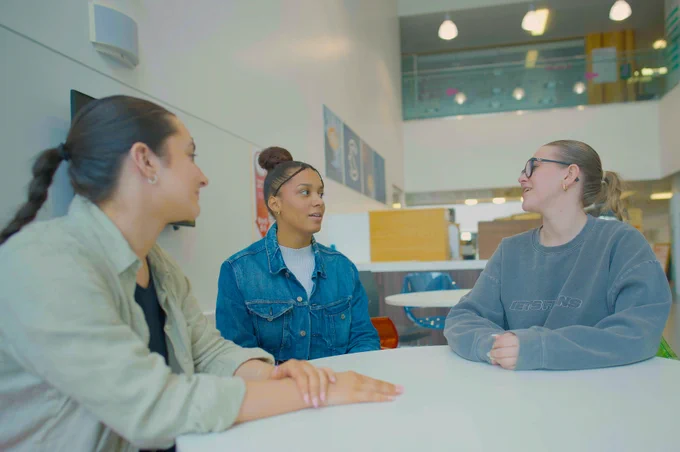 Photo of three BCU students sitting at a table and chatting