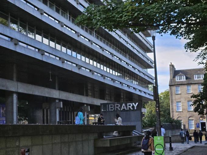 Photo of the front of Main Library showing the large Library sign with students sitting out front and walking by.