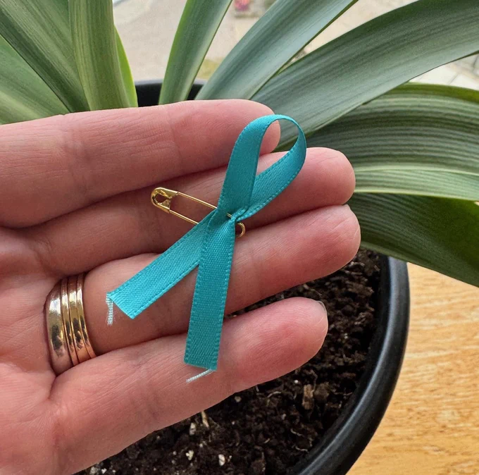 A picture of a person holding a teal color ribbon, the international symbol of sexual violence prevention.