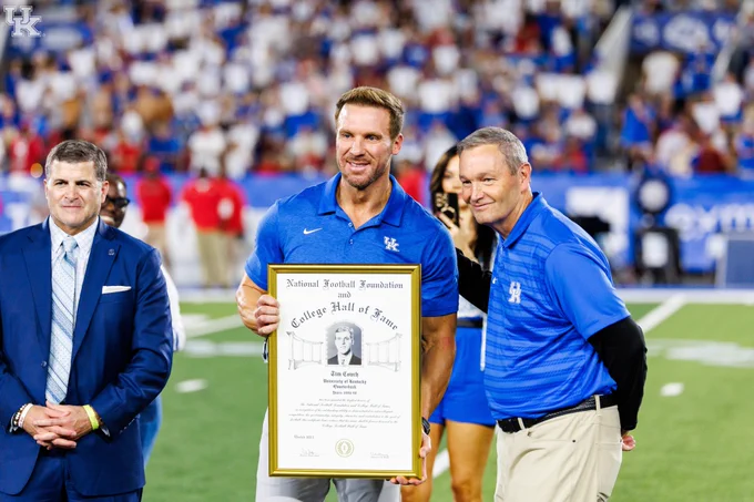 Tim Couch and Mitch Barnhart posing for a photo with an NFF and College Football Hall of Fame framed plaque. 