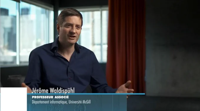 IMAGE : Capture d'écran de l'émission Découverte, montrant Jérôme Waldispühl à l'intérieur d'un édifice, parlant avec l'interviewer, qui est hors-champ à notre droite.  Son voit son nom et so titre inscrits au bas de l'image.