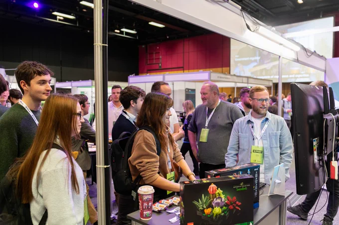 group of visitors at an exhibitors stand. A mix of men and woman with four people looking at something that is out of shot of the image but appears to be either a screen or a person they are engaging with