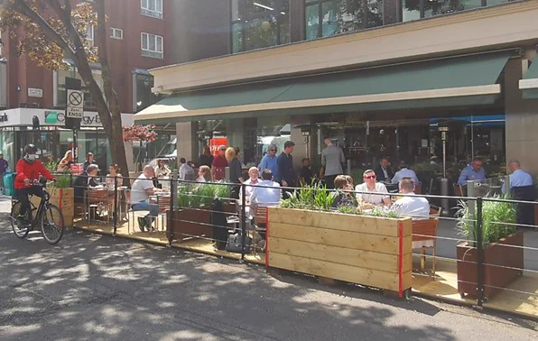 people sitting at tables in the road in an area protected by barriers
