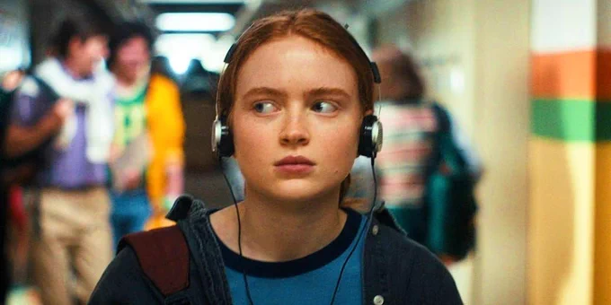 An photo of a teenager standing in what appears to be a school corridor, listening to music with over the head earphones