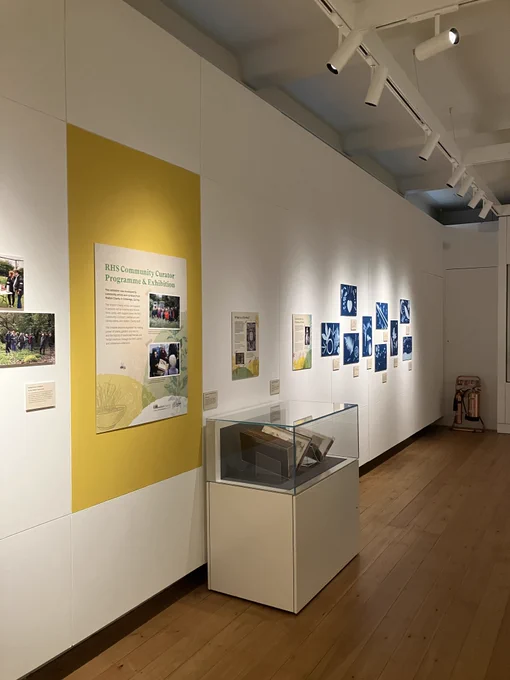The wall of an exhibition showing display panels, cyanotype photos and a rare book in a case