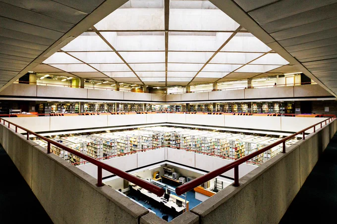 A view of the central atrium of SOAS library. Layers of book stacks overlit by skylights set in a brutalist concrete diagrid ceiling.