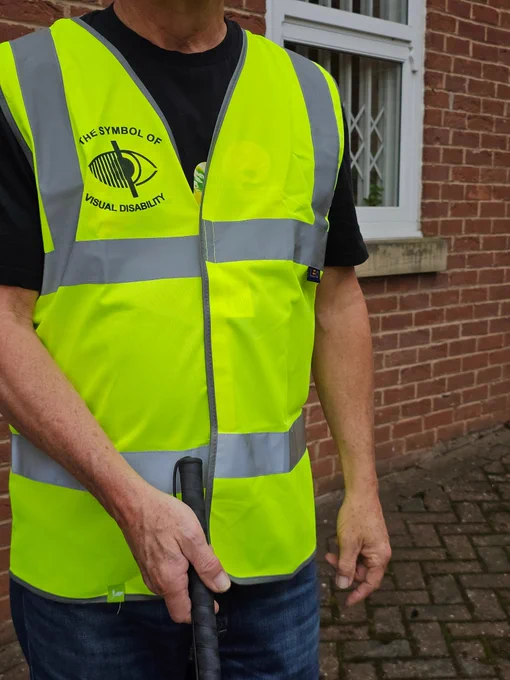 A photo of a man holding a white cane in a high visibility vest for visually impaired people.