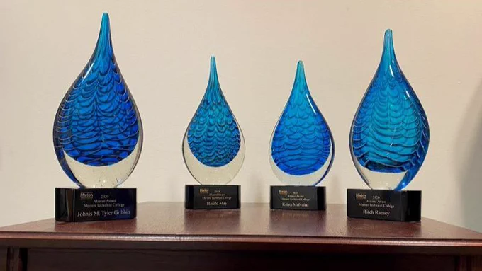 Four alumni Hall of Fame awards. they are blue glass in a tear-drop shape on a black engraved stand.