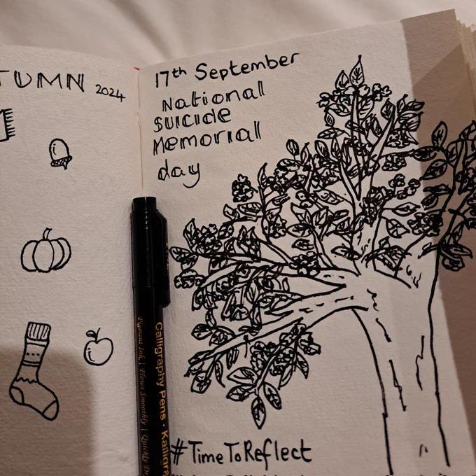 A doodle in black ink in my journal of a tree and the words 17th September, national suicide memorial day #TimeToReflect 
There is a black pen in the crease of the book and a few small autumn doodles partially visible on the other page