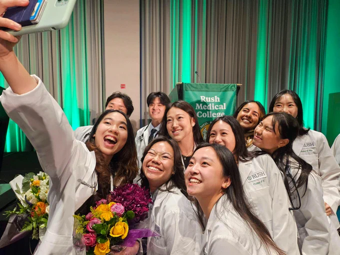 Group of Rush Medical College students in white lab coats smiling and taking a selfie at the white coat ceremony.