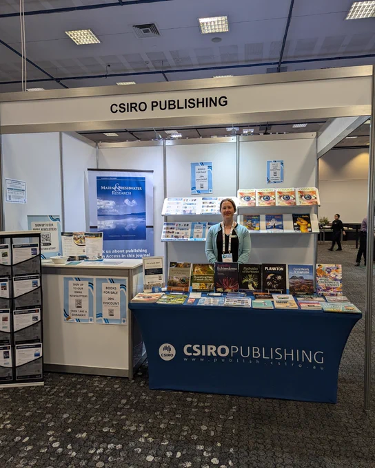 Eloise Moir-Ford smiles, standing at the CSIRO Publishing conference booth behind a table full of books.